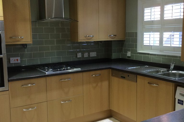 Oak effect kitchen cupboards with a a black stone laminate worktop & up stand.